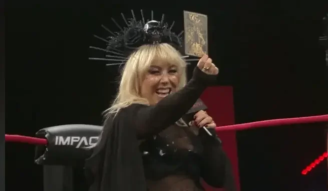aylor Wilde wearing a black crown with skull and rose accents, holding up a tarot card in a wrestling ring.