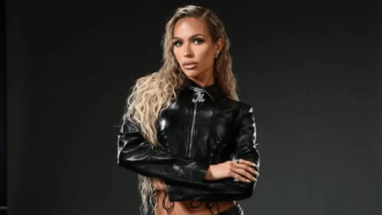 WWE superstar Maxxine Dupri posing with arms crossed in a black leather jacket against a dark background.