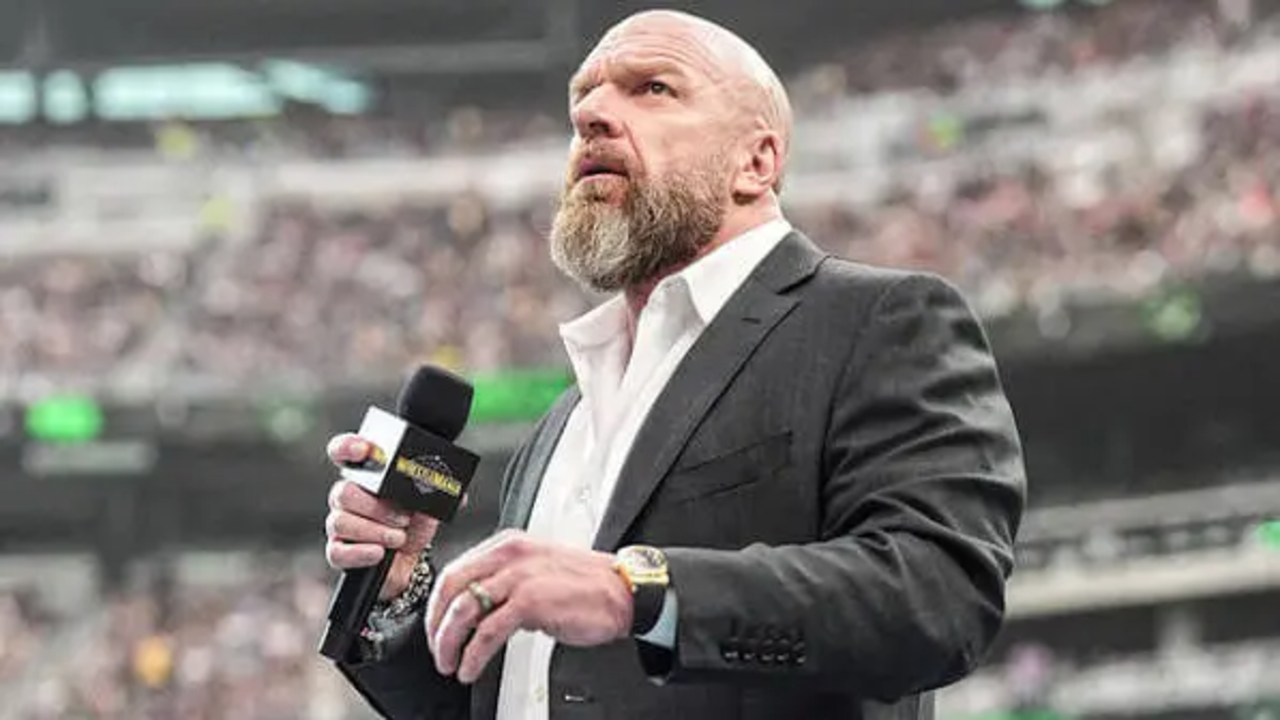 Triple H with a microphone in his hand, standing in a ring with a huge amount of fans in the arena.