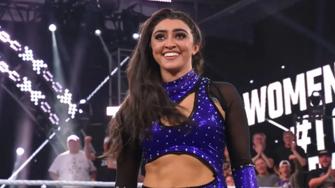 Wren Sinclair smiling in the ring after winning the NXT Women’s Championship #1 Contender’s Battle Royal, wearing a sparkling blue high-neck crop top with sheer sleeves