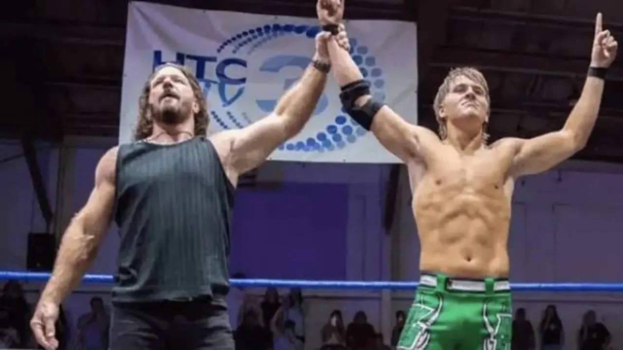 AJ Styles holding up the arm of his son Avery Styles in a wrestling ring, sparking indie scene debates.