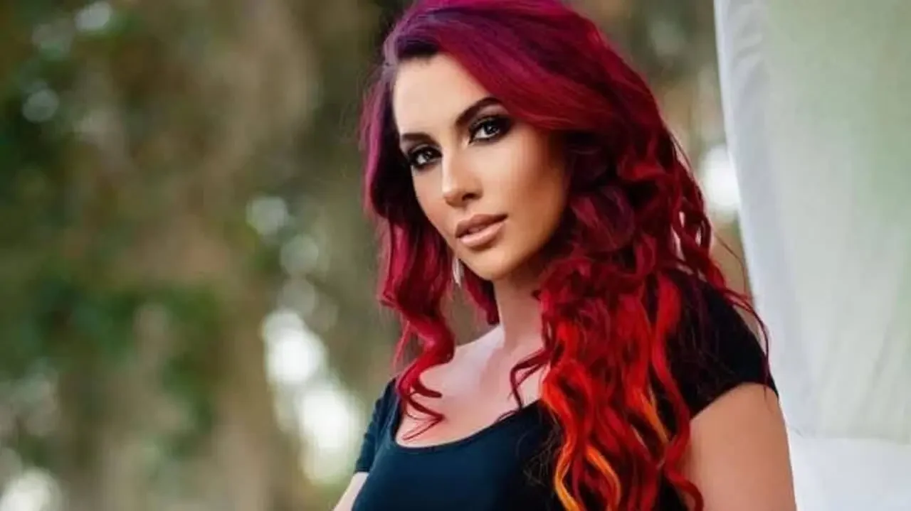 Santana Garrett with vibrant red hair wearing a dark top against a light outdoor backdrop.