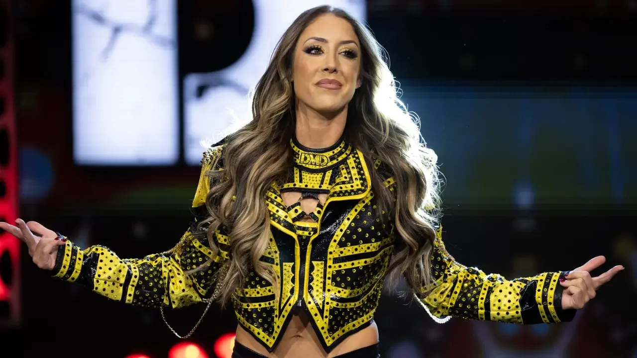Britt Baker wearing her black and yellow gear with arms outstretched during her return.
