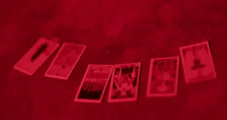 A spread of tarot cards laid out under a dark, red-lit atmosphere.
