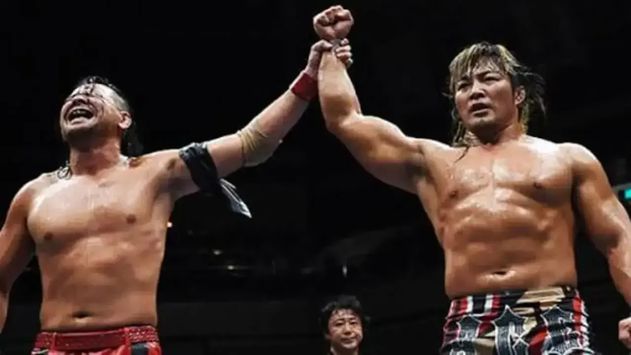 Shinsuke Nakamura and Hiroshi Tanahashi standing victorious together in a New Japan Pro-Wrestling ring, holding each other's hands high.