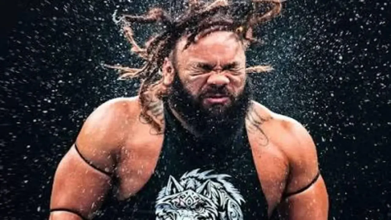 Jacob Fatu with dreadlocks and a beard, wearing a black graphic tank top, shaking water droplets off his head in an intense, explosive motion against a dark background.