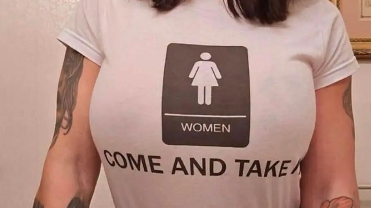 Woman wearing a white t-shirt with a women’s restroom symbol and the text “COME AND TAKE IT”