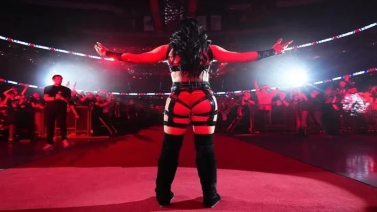 Stephanie Vaquer standing on the stage facing away from the camera with arms outstretched under arena lights