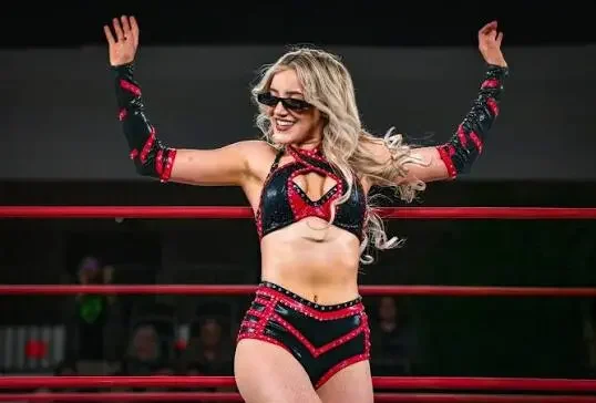 A medium shot photograph of the professional wrestler Zayda Steel standing inside a wrestling ring, leaning against the top rope.