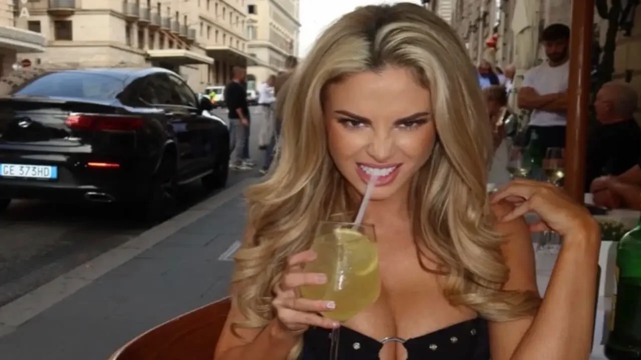Harley Cameron sitting at an outdoor European cafe sipping a drink with a straw while posing for the camera.