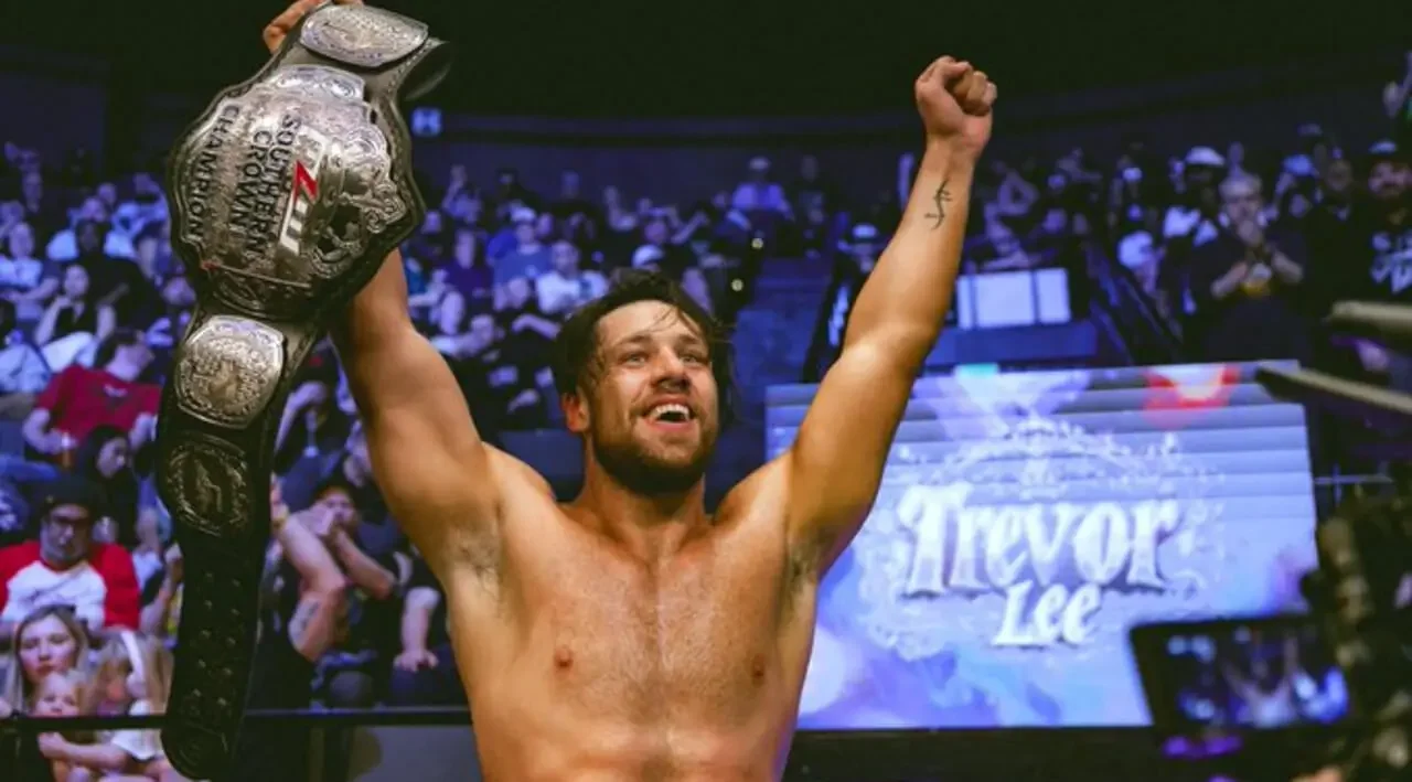 A smiling Trevor Lee is in a professional wrestling ring, holding the MLW Southern Crown Championship high in his right hand.