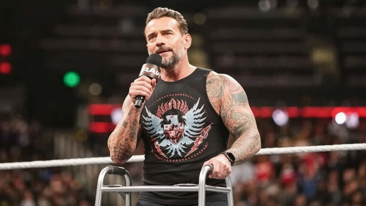 vCM Punk standing in a WWE wrestling ring, holding a microphone in his right hand and gripping the handles of a silver metal walker with his left hand.