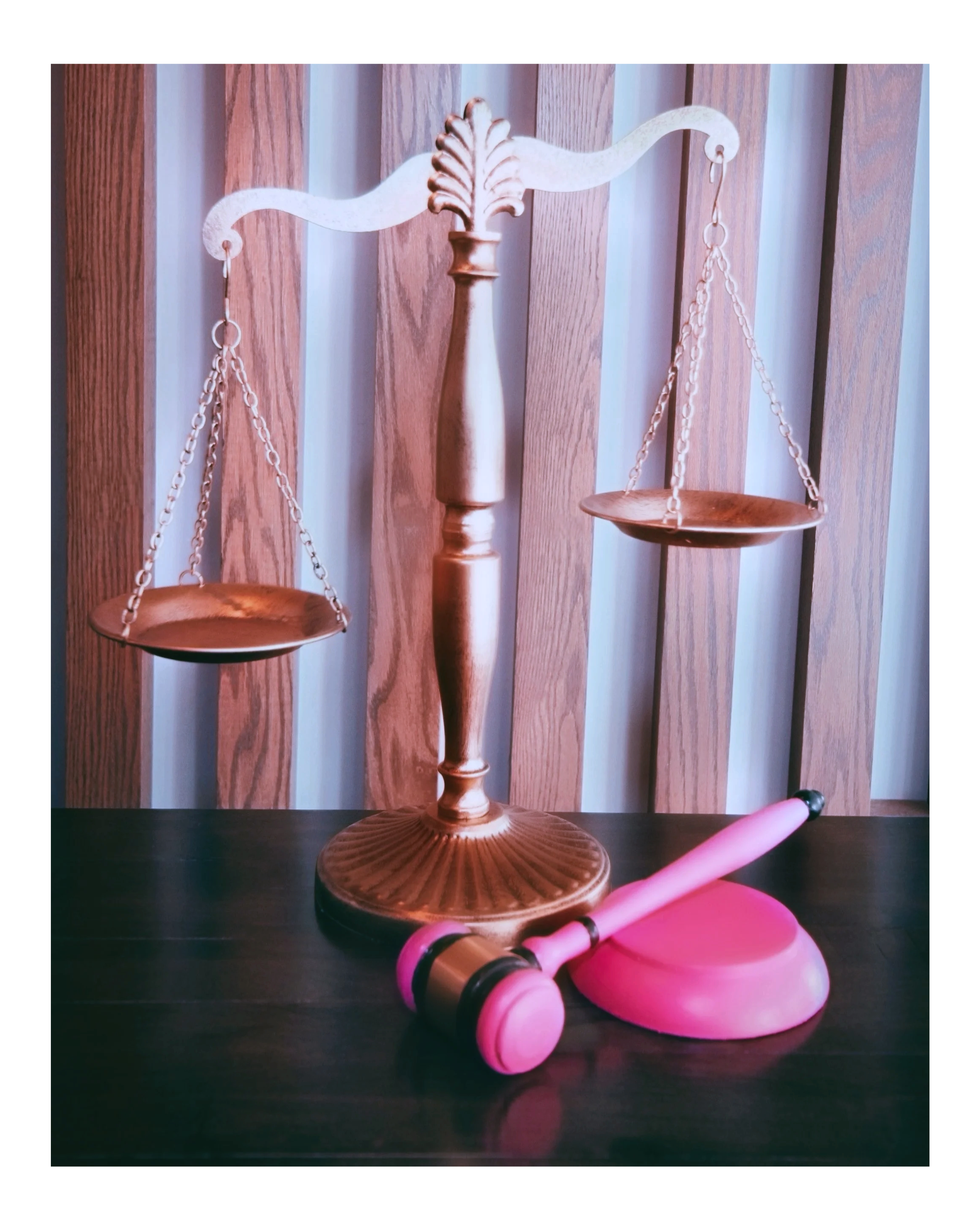an imbalanced scales of justice next to a pink and brown gavel.