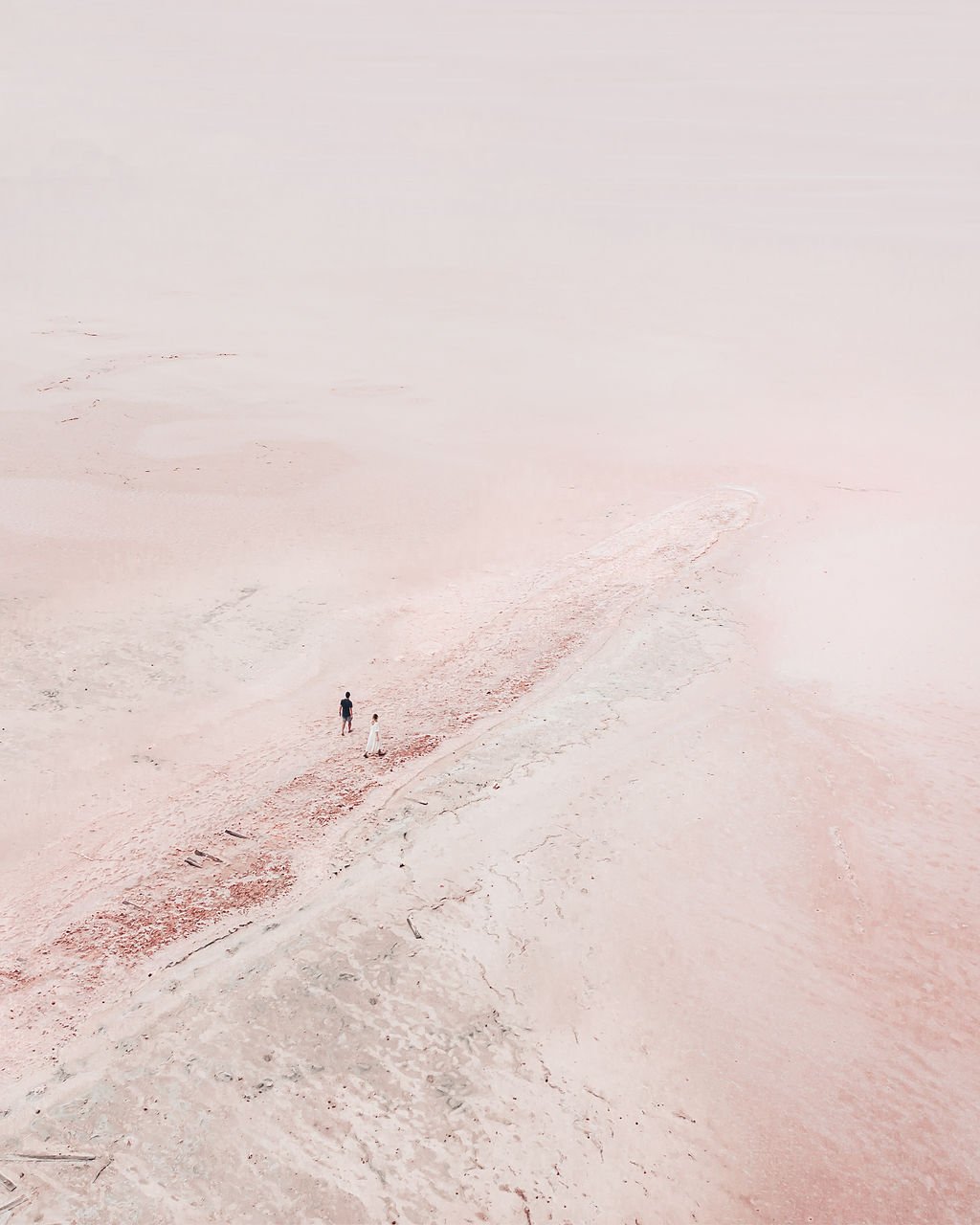 A vast, pale pink sandy beach with two small figures walking along the shoreline.