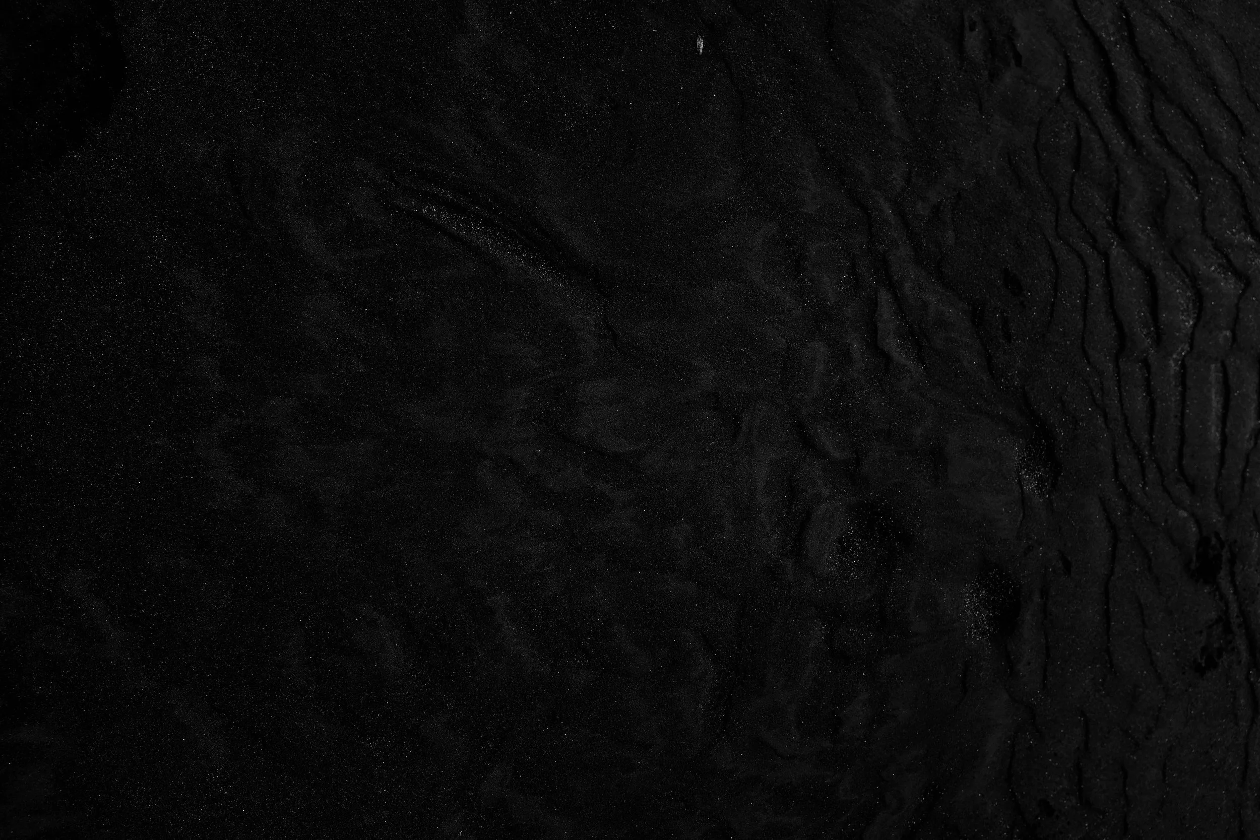 Close-up of black textured surface with wavy patterns and small sparkling particles.