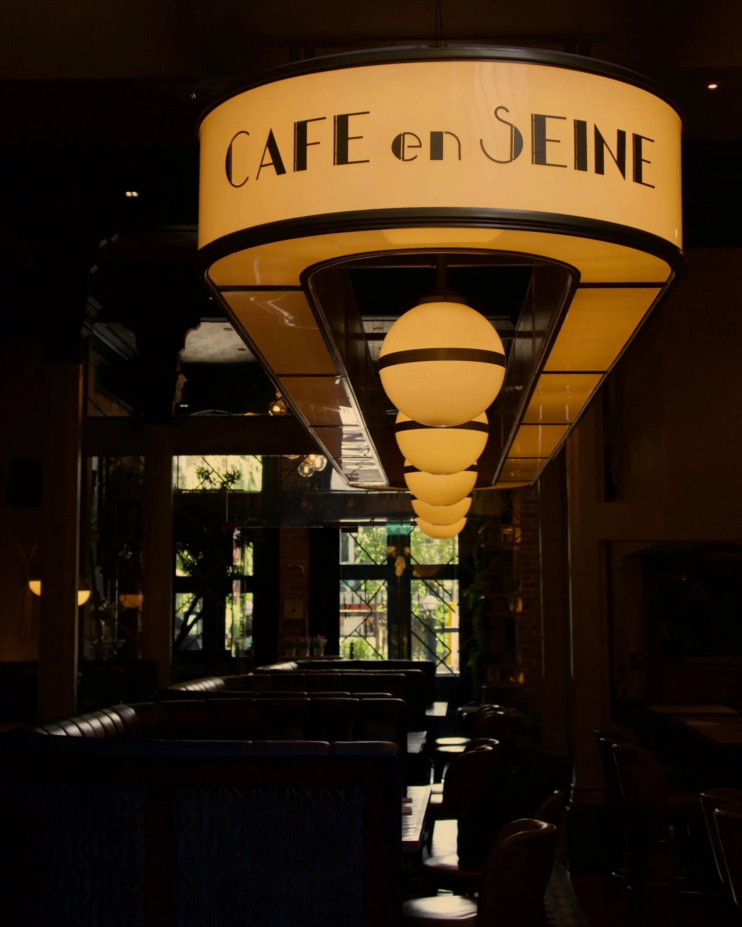 Dimly lit restaurant interior with candles on tables and large windows showing greenery outside.