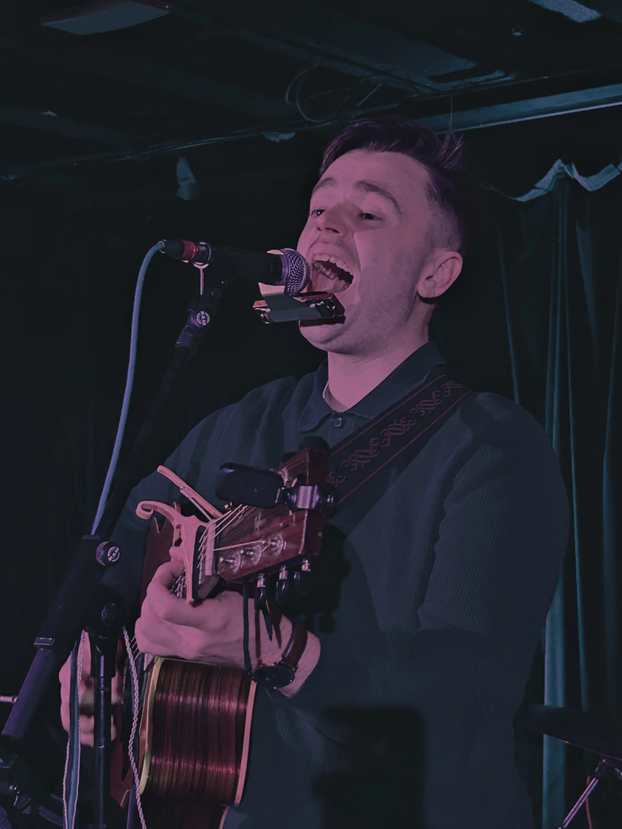 A man singing into a microphone while playing an acoustic guitar during a performance.