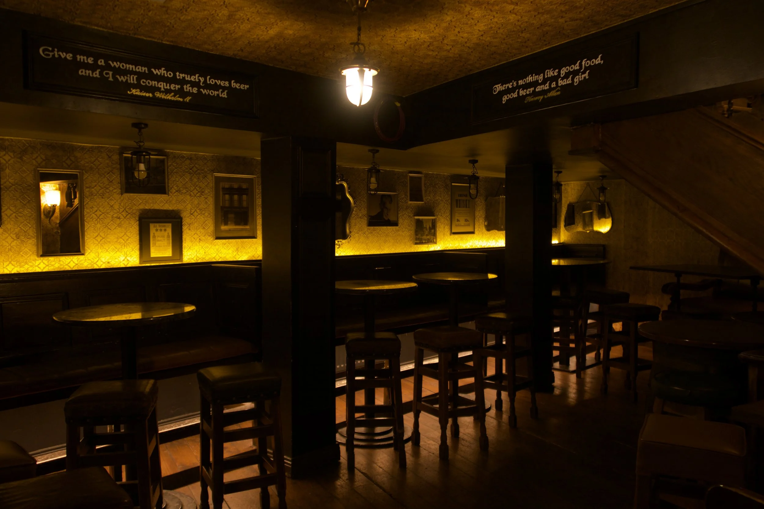 A dimly lit interior of a restaurant or cafe with wooden walls, a window showing a brick building outside, a booth with a beige cushioned bench, and a table with yellow candles.