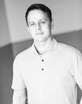 Black and white portrait of a young man in a short-sleeved collared shirt, looking at the camera with a slight smile.