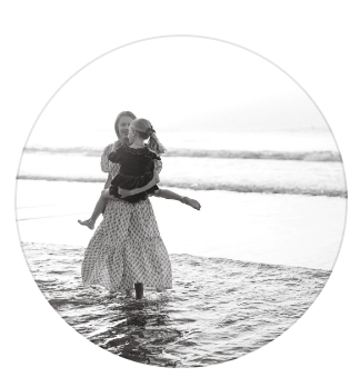 A woman holding a child at the beach with gentle waves in the background, black and white photo