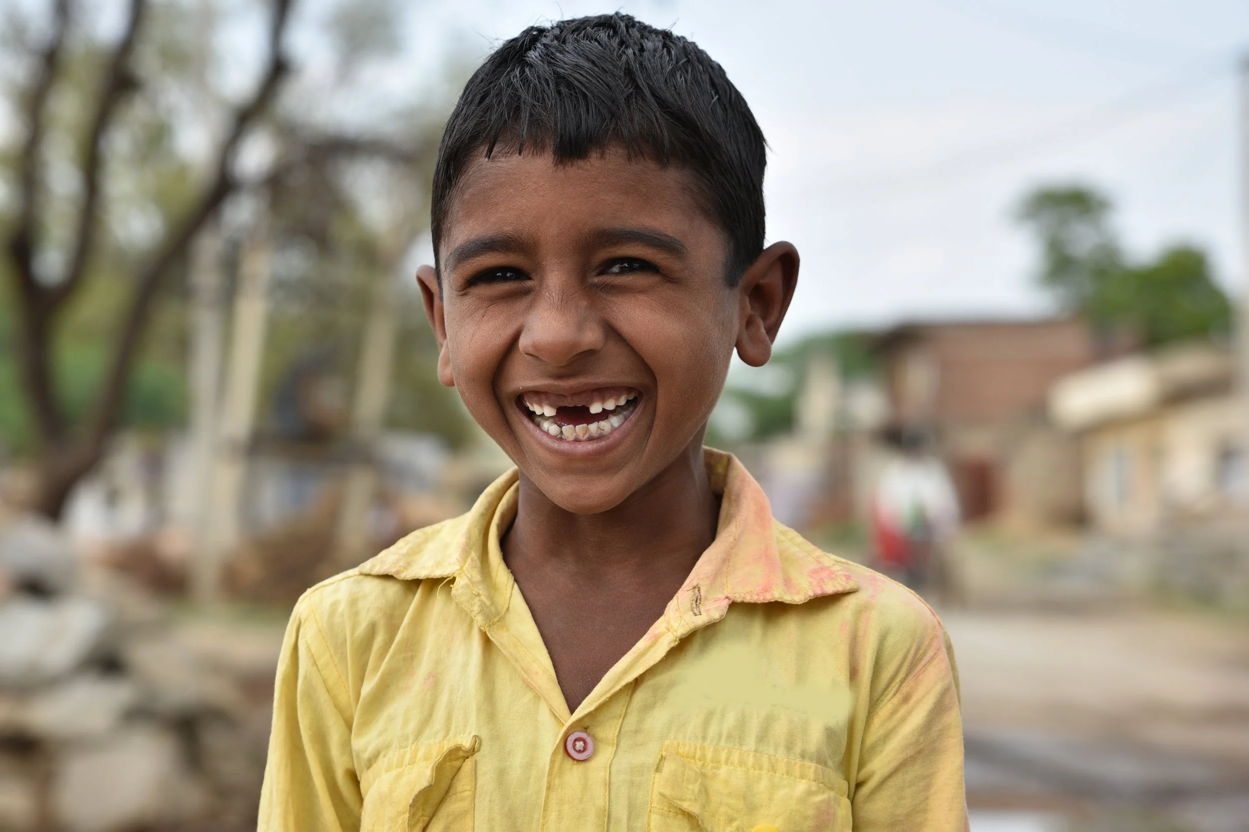 A smiling young boy in a yellow shirt.
