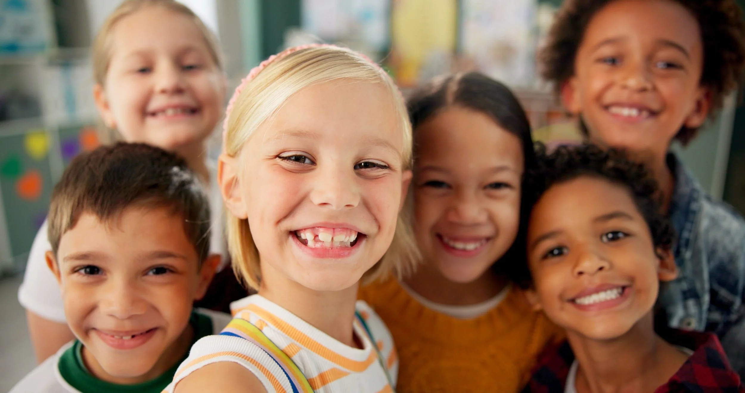 Group of smiling diverse children taking a close-up selfie in a classroom.
