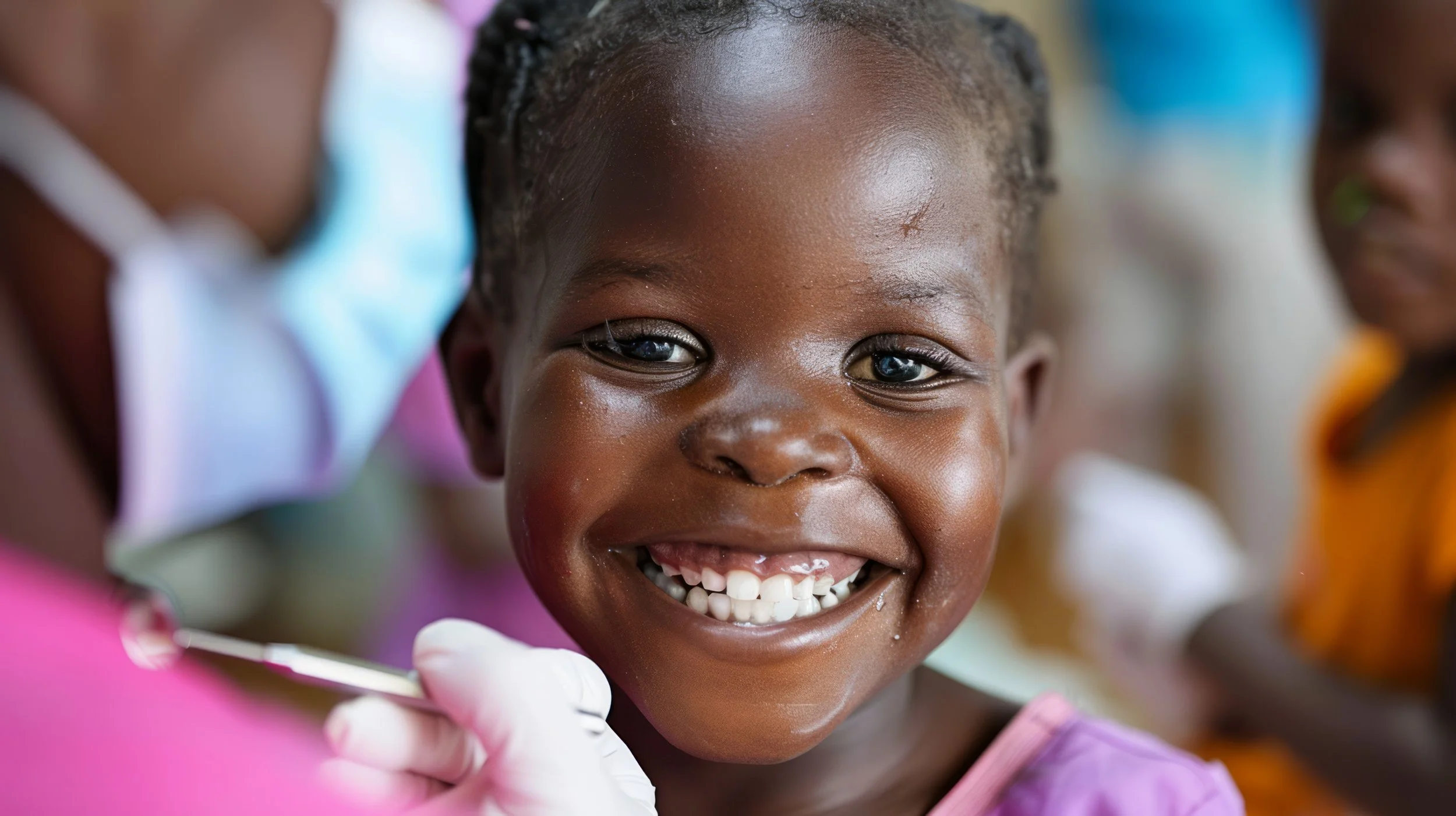 A young African girl with a big smile, showing missing teeth, as she receives dental treatment from a healthcare worker wearing gloves.