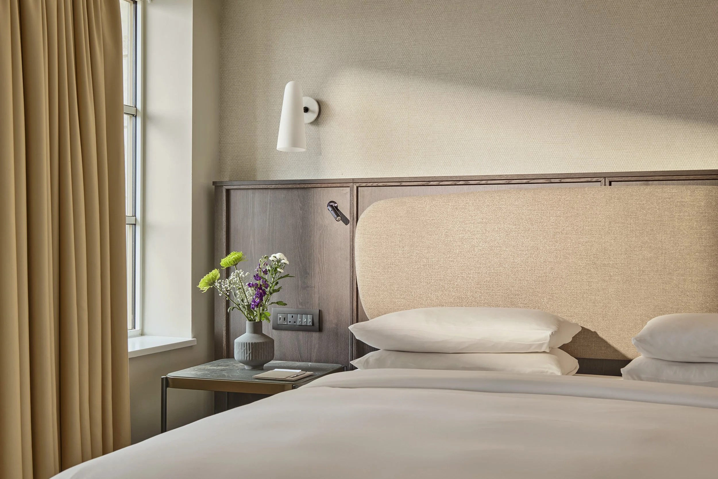 Two women holding pinkish-orange cocktails with black straws sitting at a speckled table in a restaurant.