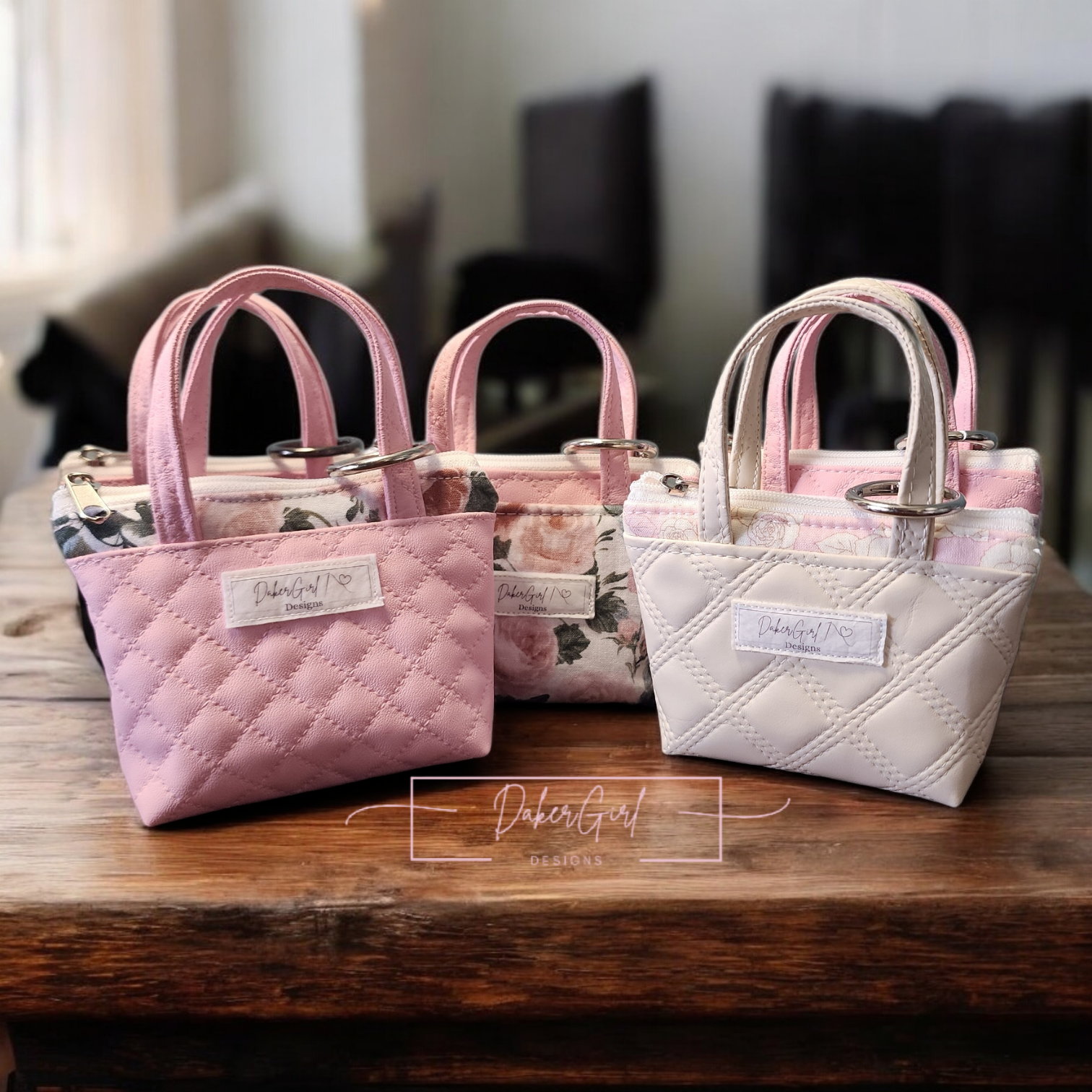 Small quilted handbag keychain with handles and tags, in pink, floral, and white, displayed on a wooden surface.