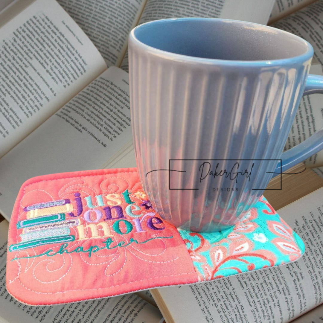 A ceramic mug resting on a colorful fabric coaster with embroidered text and books open in the background.