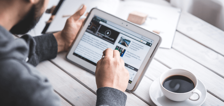 Person reading news or analyzing data on a tablet with a cup of coffee, representing social media strategy and digital marketing research services in Cork.