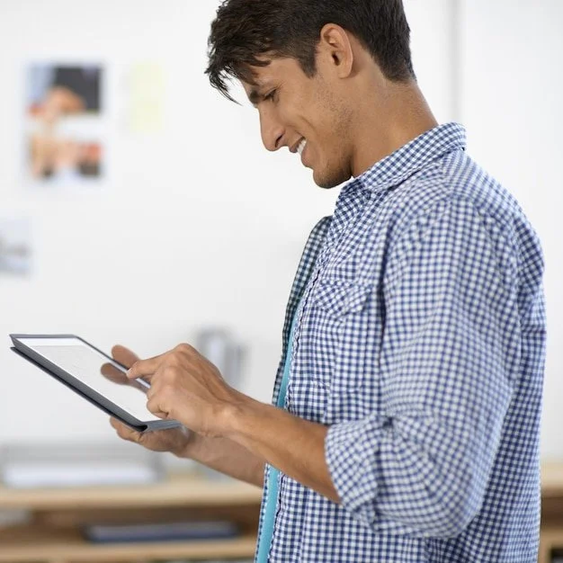 A smiling professional standing in an office and reviewing a digital strategy on a tablet device.
