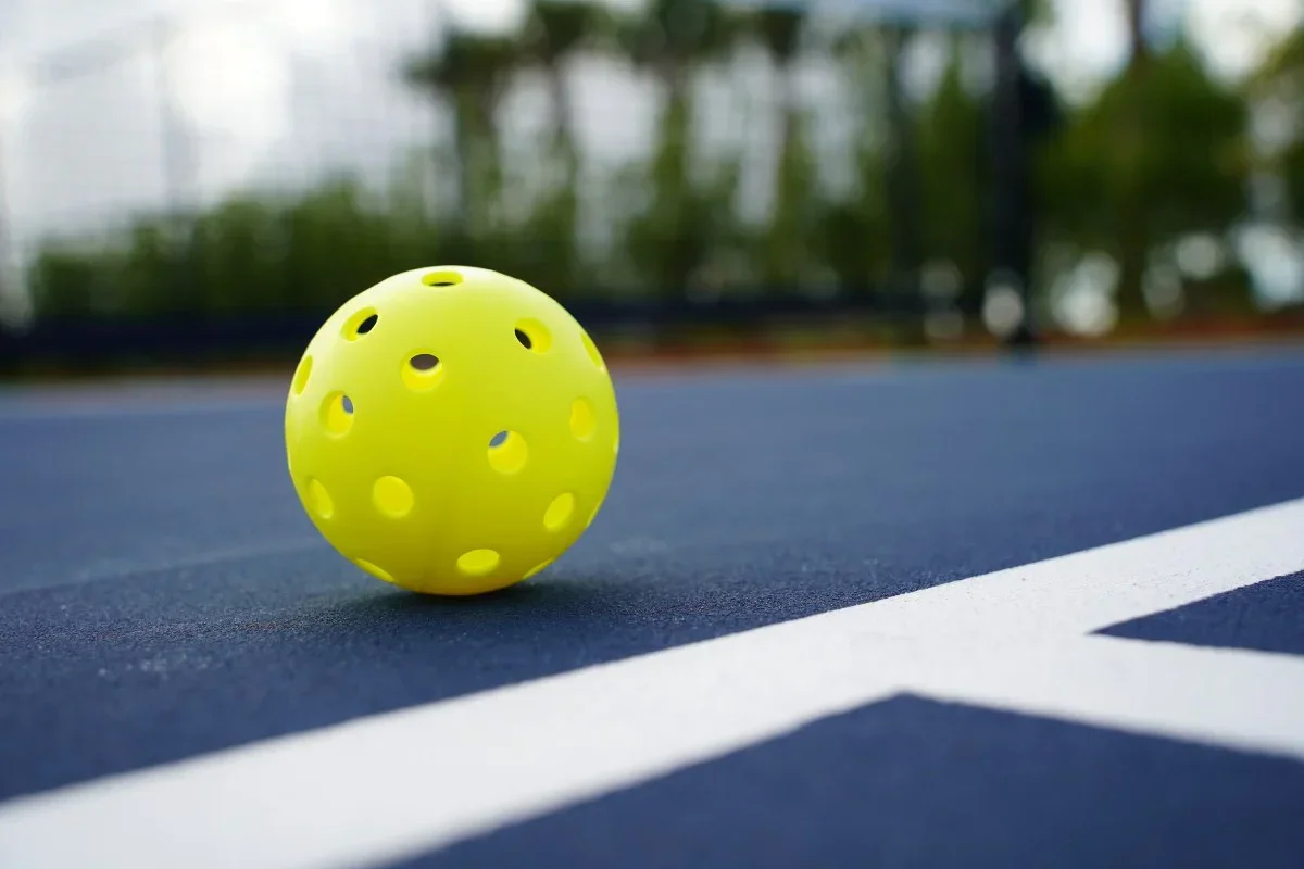 A yellow perforated ball on a tennis court.