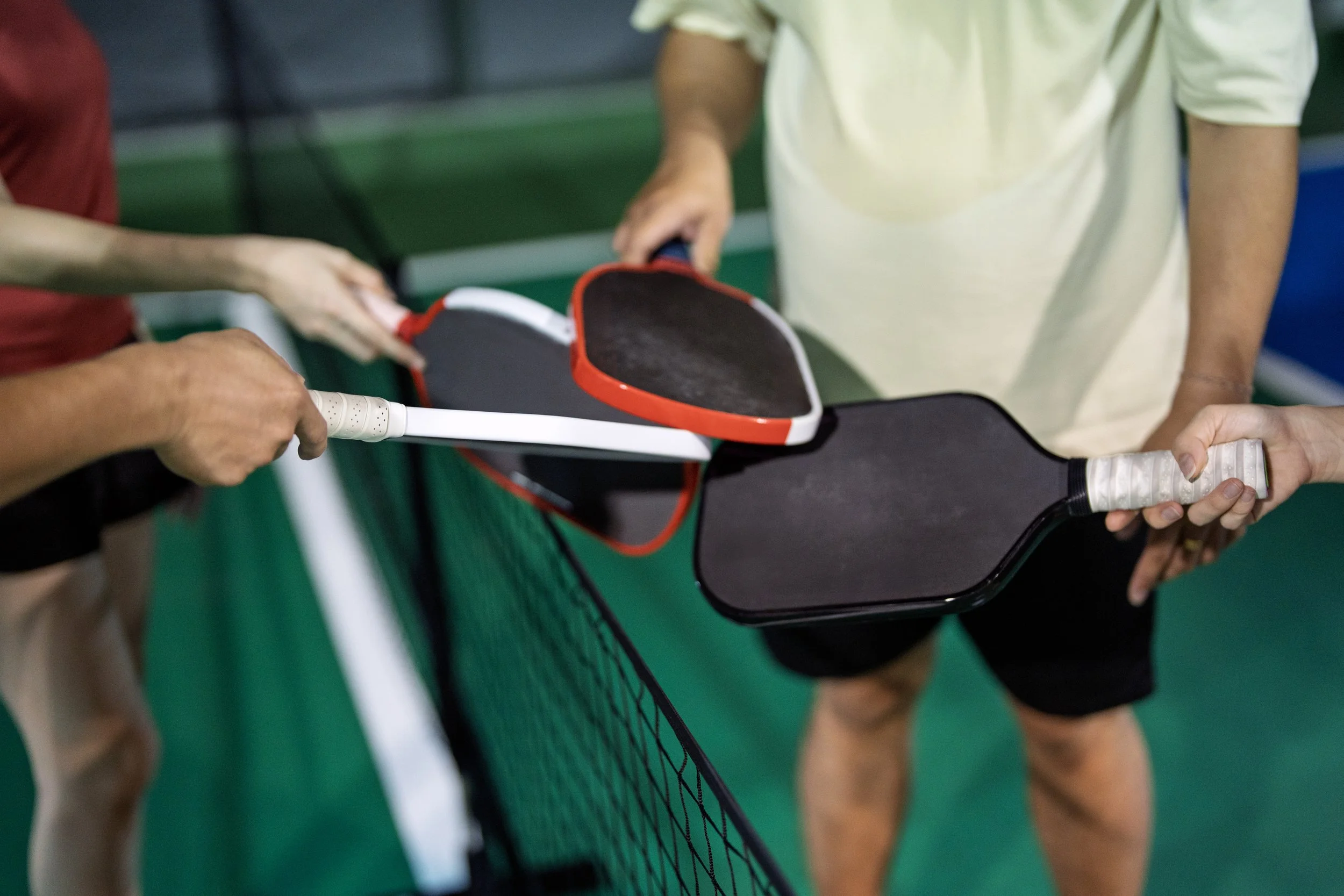 People exchanging pickleball paddles and ball at an indoor court.