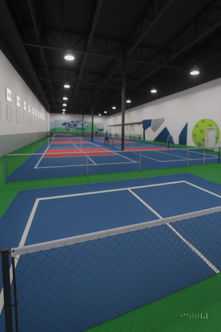 Indoor tennis courts with blue surfaces, white lines, and a green border, inside a large, well-lit sports facility.
