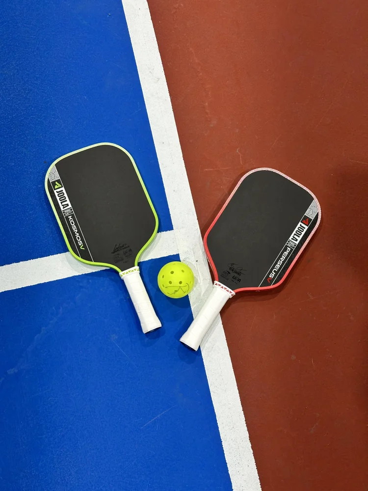 Two pickleball paddles and a ball on a Rockii court