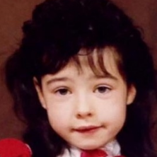 A young child with dark, curly hair and light skin, smiling slightly at the camera.