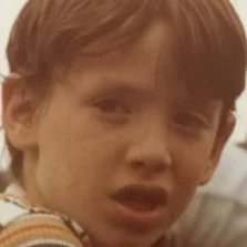 Close-up of a young boy with brown hair and a confused or surprised expression.
