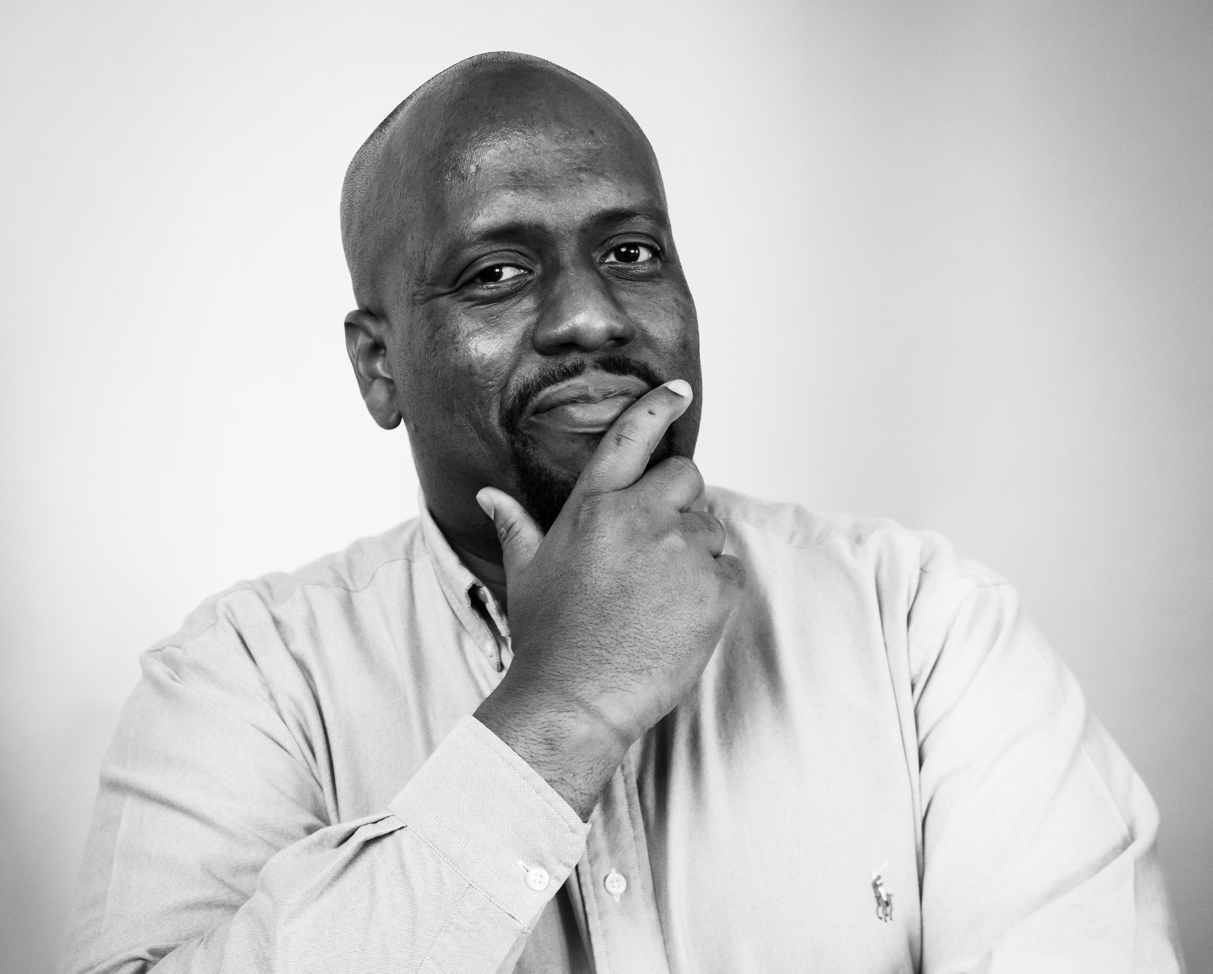 Black and white portrait of a man with a thoughtful expression, wearing a collared shirt and resting his chin on his hand.