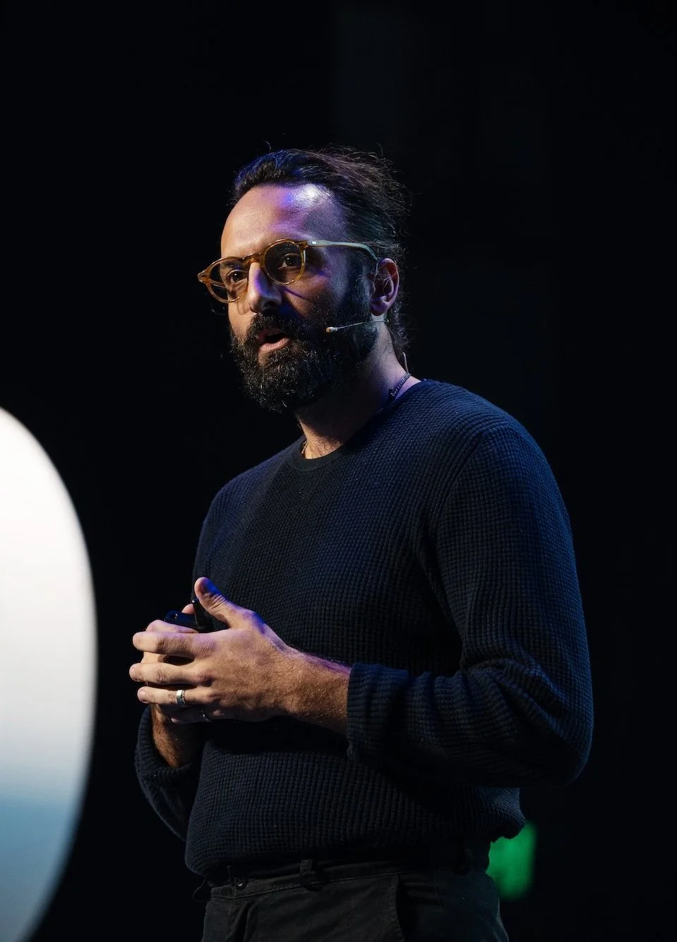 A man with glasses and a beard giving a presentation on a dark stage.