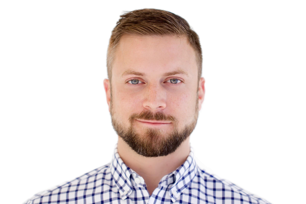 Headshot of a man with short red hair and a beard, wearing a checkered shirt, against a white background.