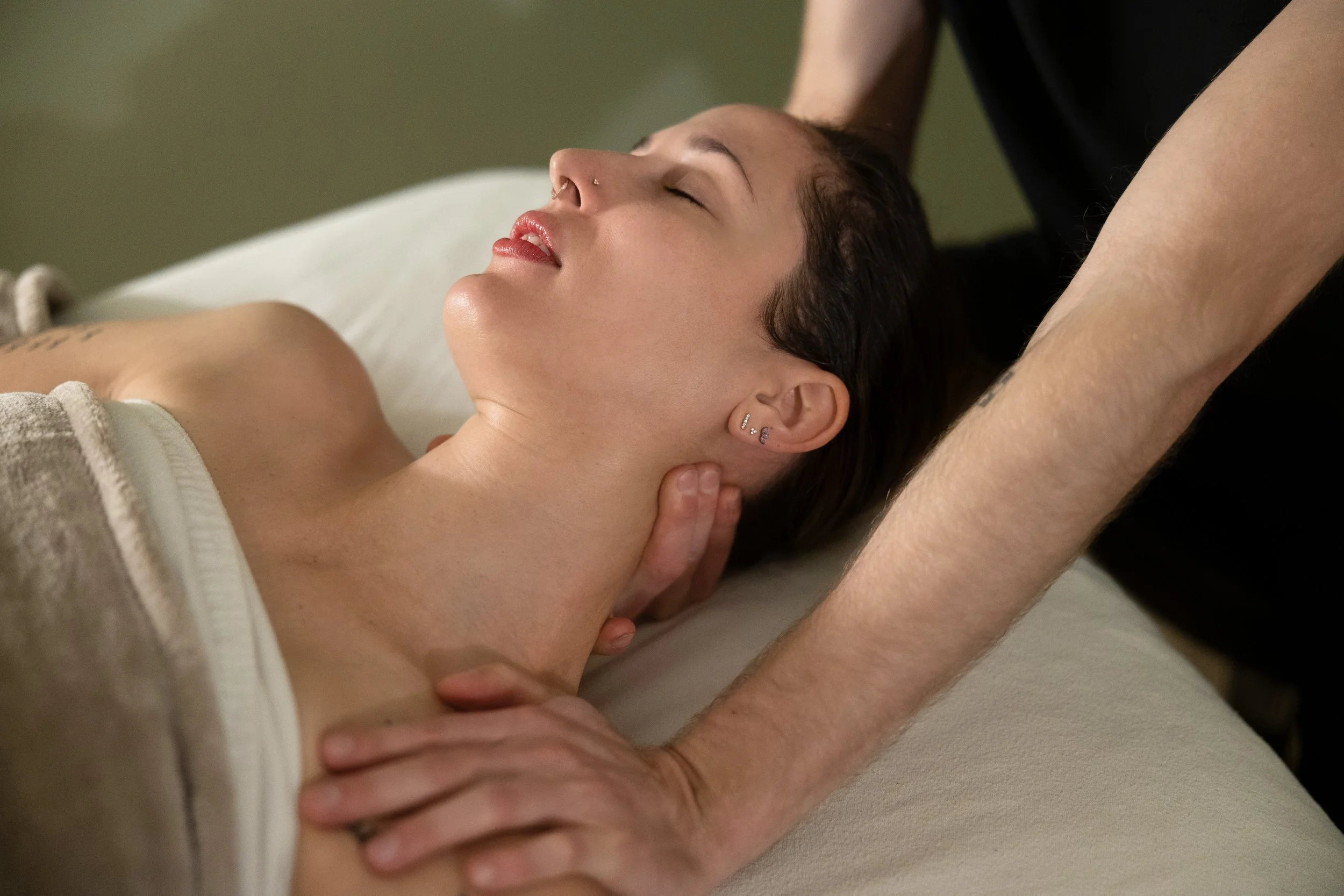 Person receiving a neck massage while lying down with eyes closed, and a massage therapist's hands on their neck.