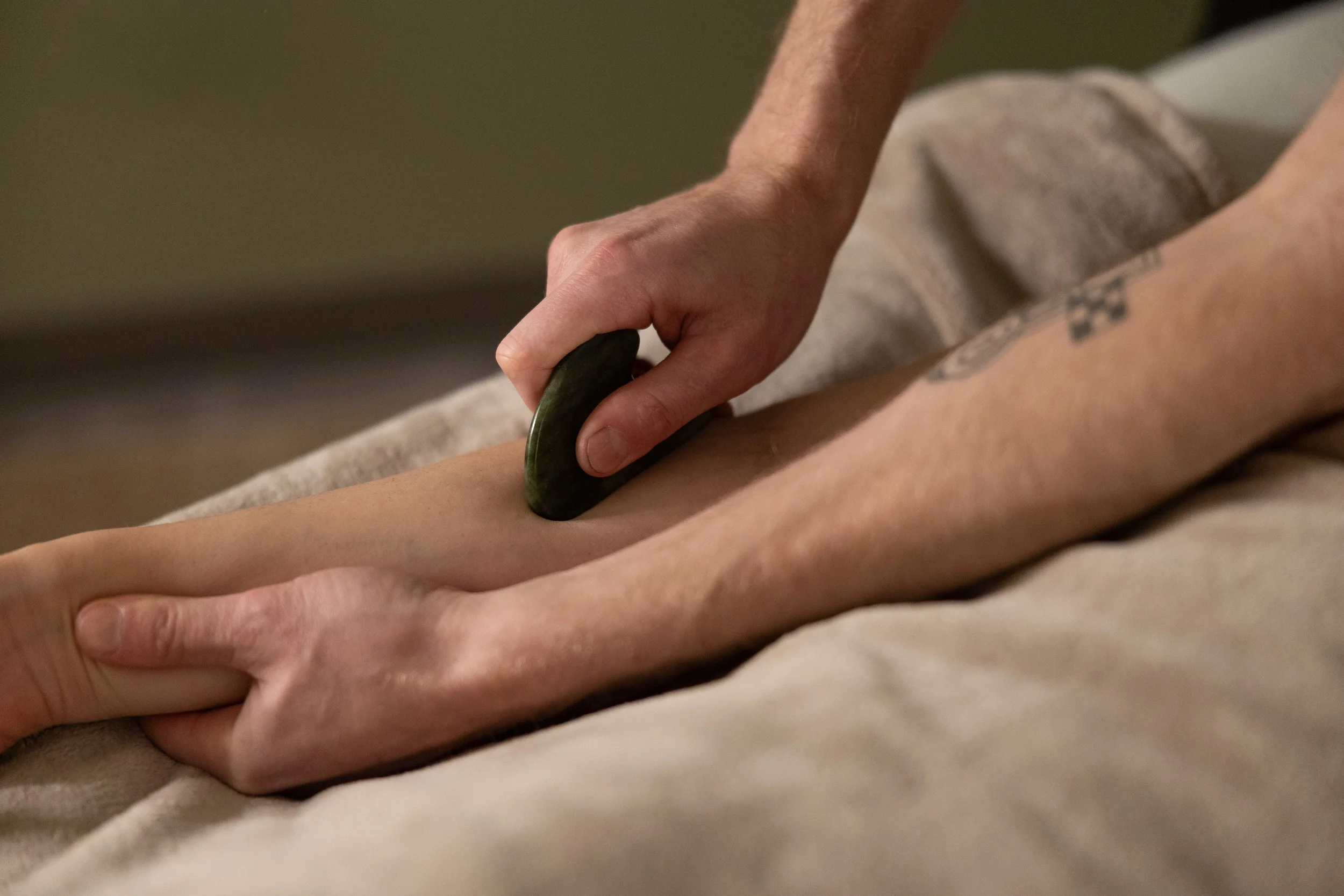 Person receiving a hot stone massage, with a masseuse applying a smooth, heated stone to their forearm.