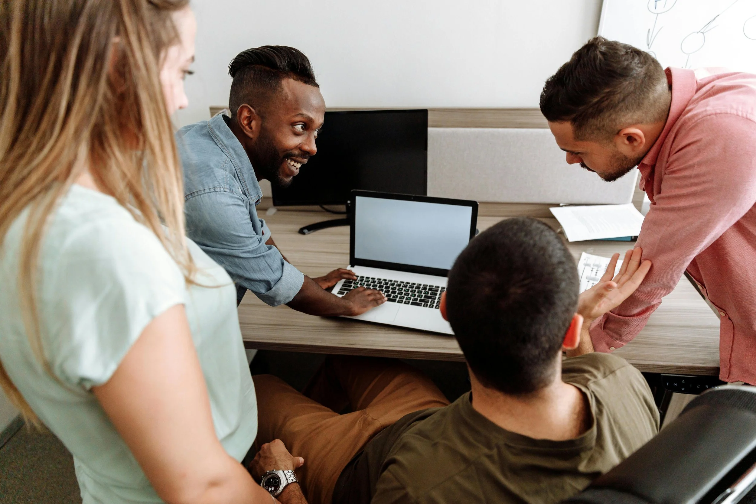 Group of four coworkers discussing around a laptop in an office