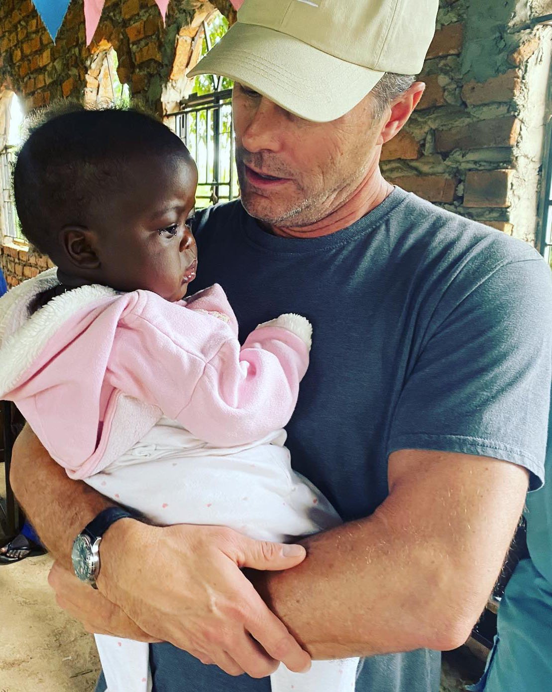 A man holding a young girl inside a building with brick walls and windows.