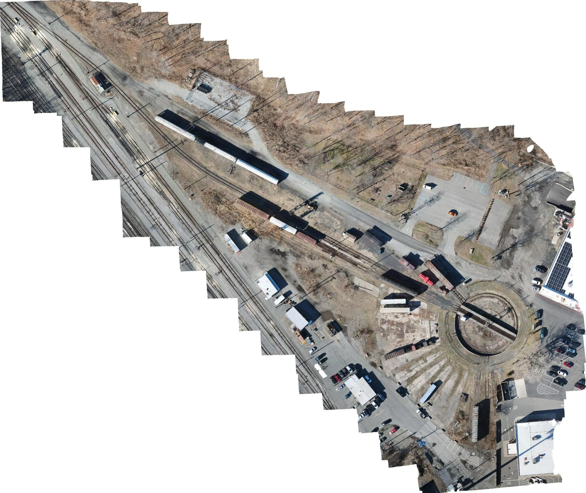 Aerial orthomosaic of a train yard with multiple train tracks, parking lot, and surrounding barren trees and buildings.