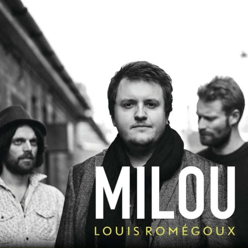 Black and white band photo of three men, with the central man in focus, wearing a blazer and a scarf, with the name 'Milou' and 'Louis Romégoux' written on the image.