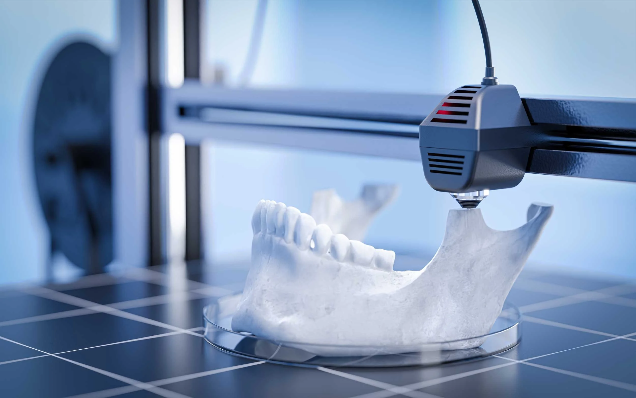 A 3D printer printing a model of a human jawbone on a black tiled surface.