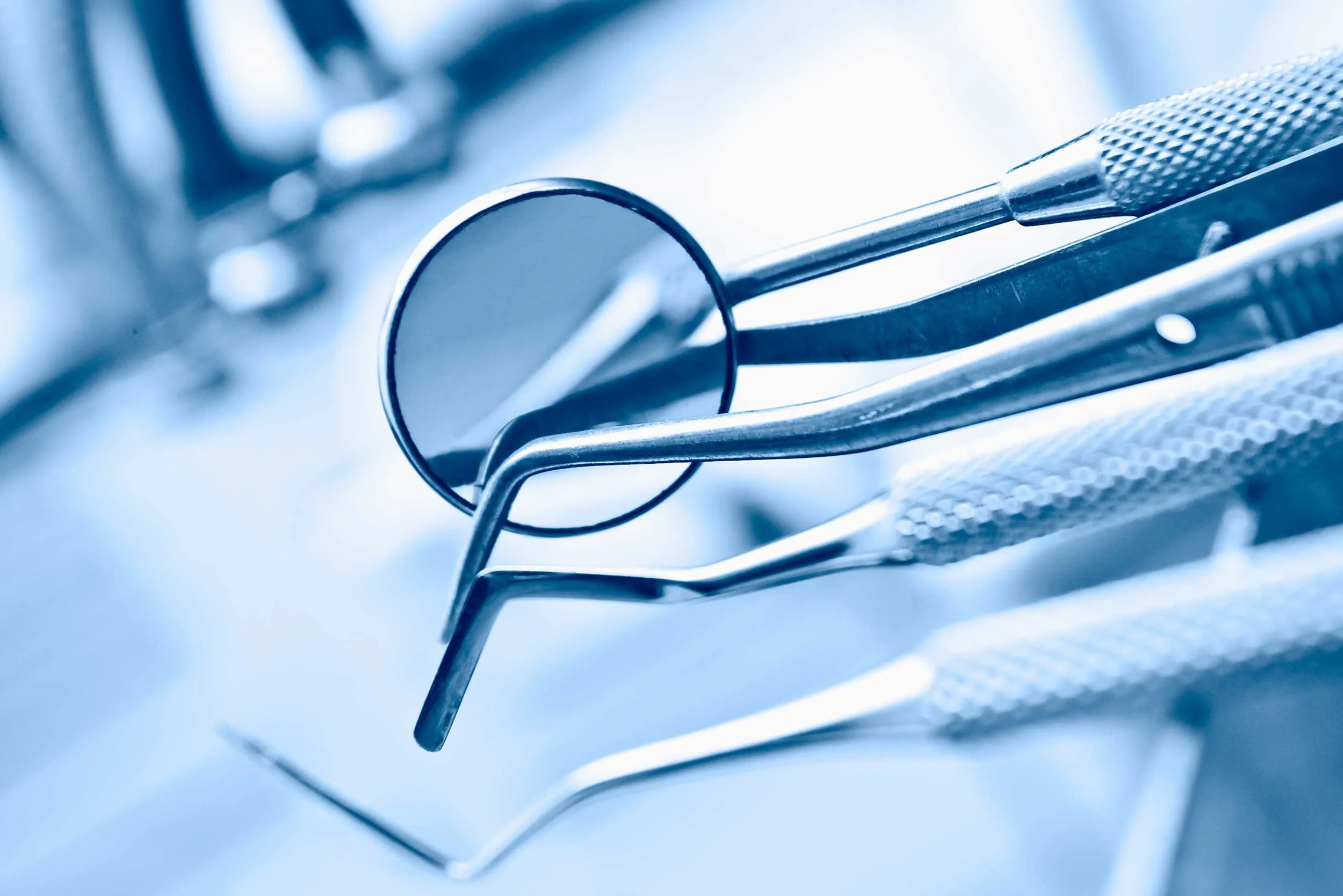 Close-up of dental tools, including a mirror, dental pick, and scaler, arranged on a clinical surface.