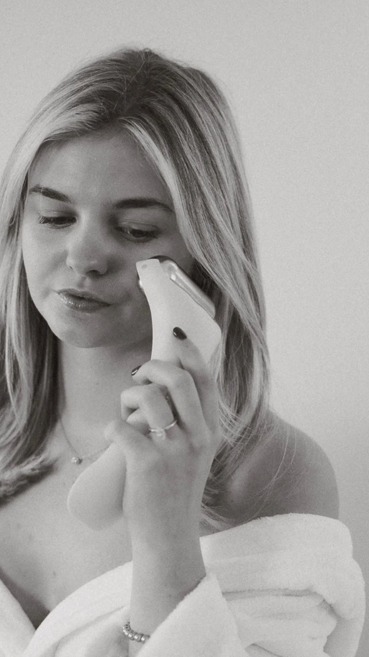 A woman in a robe looking downwards using an ice roller to de-puff her face, black and white photo.
